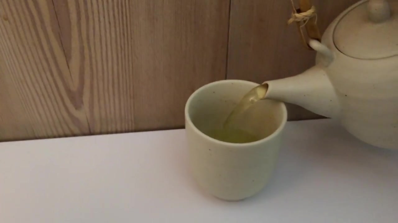 Hot green tea poured into a white cup beside a ramen bowl