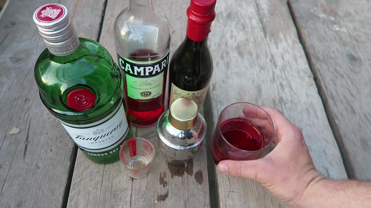 The red Negroni in a glass beside the bottles and cocktail equipment.