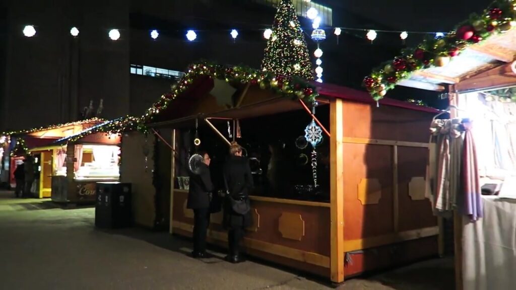 Wooden Christmas market chalets decorated with lights outside Tate Modern