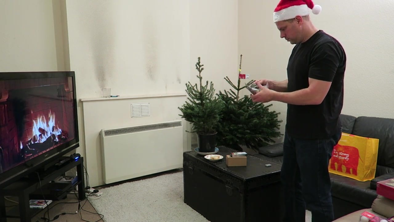 Barry in a Santa hat beside an undecorated Christmas tree in the living room.