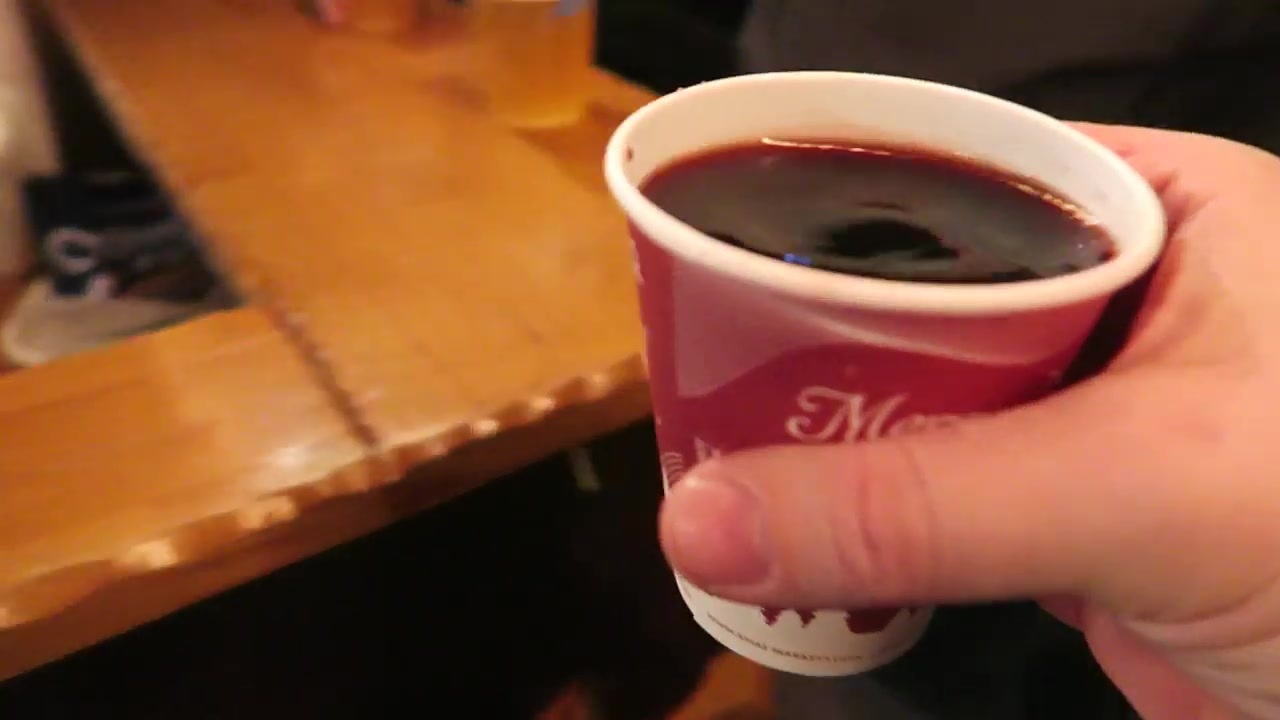 A cup of red mulled wine held beside a wooden market counter