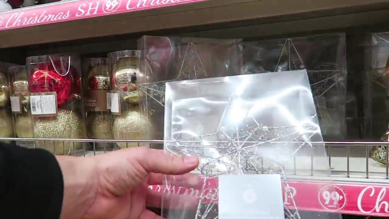 A hand holding a packaged silver star tree topper in the Christmas aisle