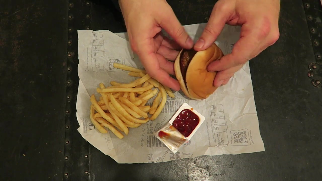 Hands opening a hamburger beside fries and ketchup on a wrapper