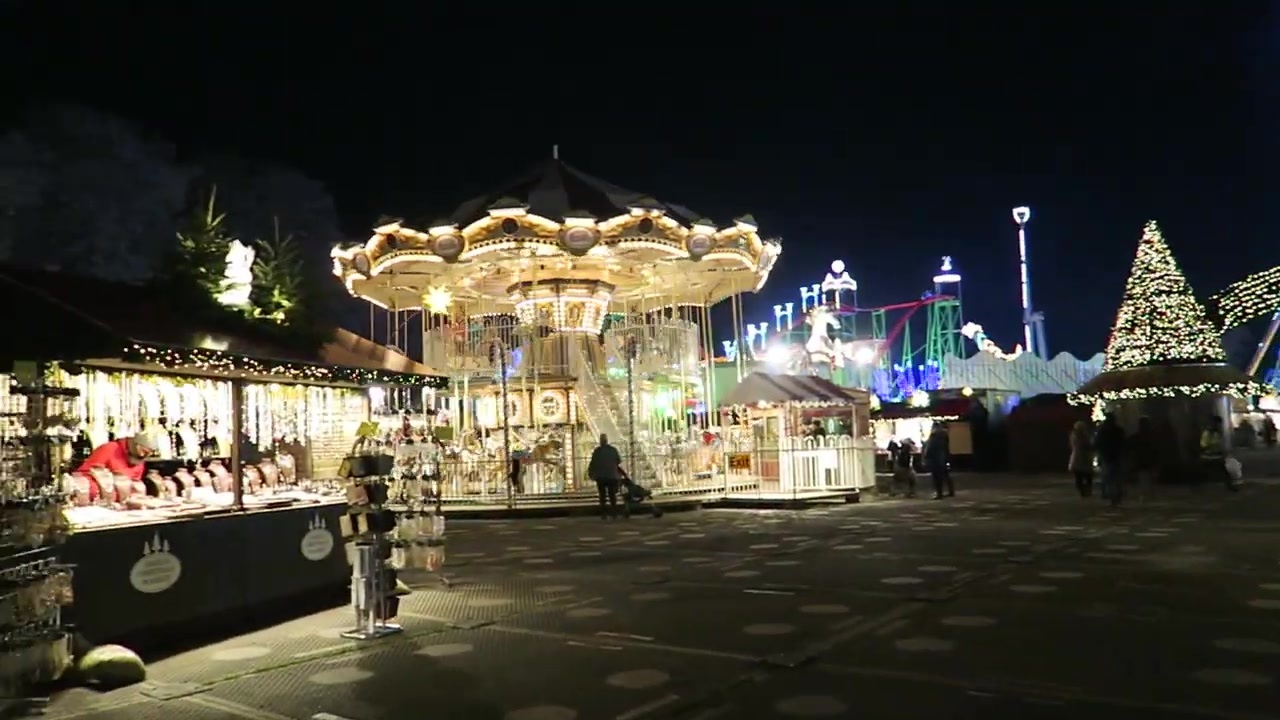 Illuminated carousel beside Christmas market stalls after dark