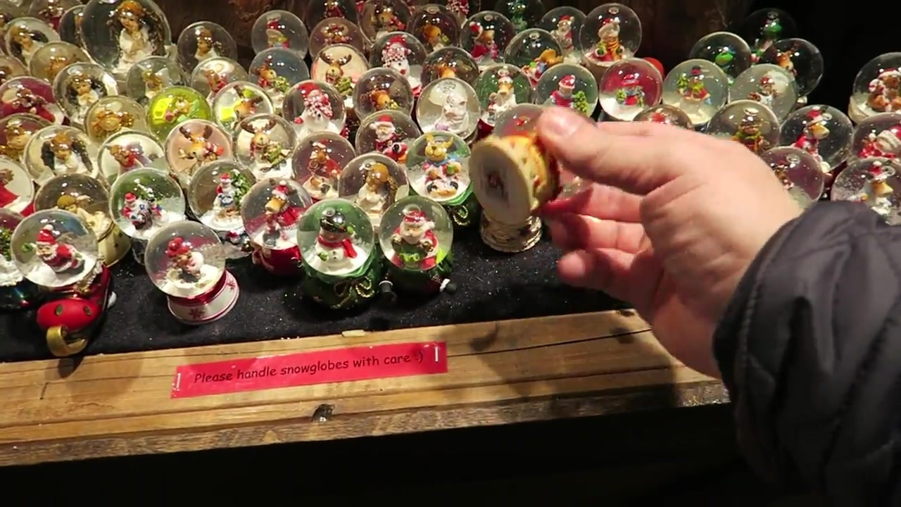 A hand holding a small snow globe above a Christmas stall display