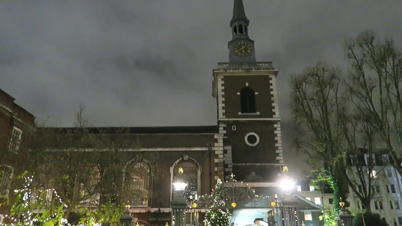 Church tower above trees and Christmas lights at night