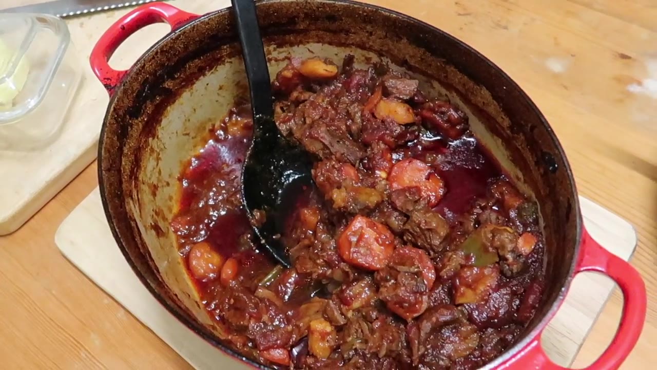 Slow-cooked beef and root vegetable stew in a red casserole dish