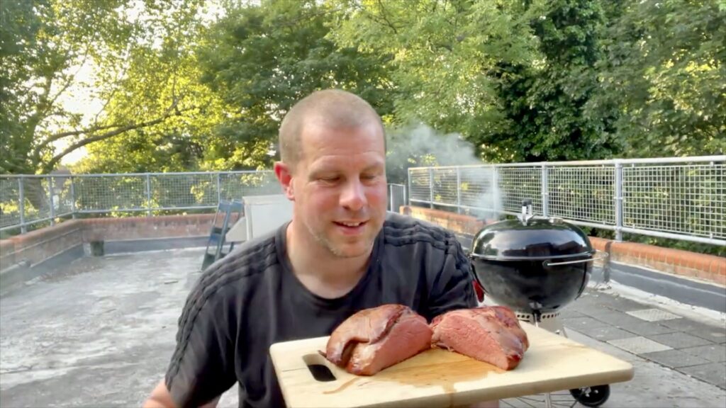 Finished oak and rosemary smoked lamb resting on a wooden board beside the barbecue