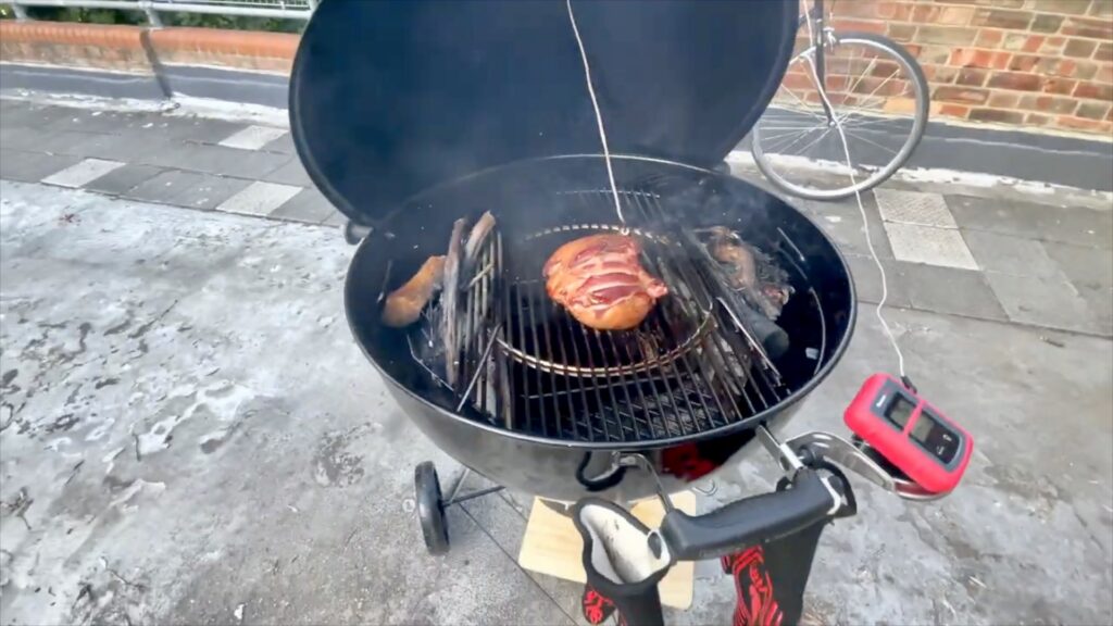 Smoke rising around lamb inside a Weber kettle barbecue on a London rooftop