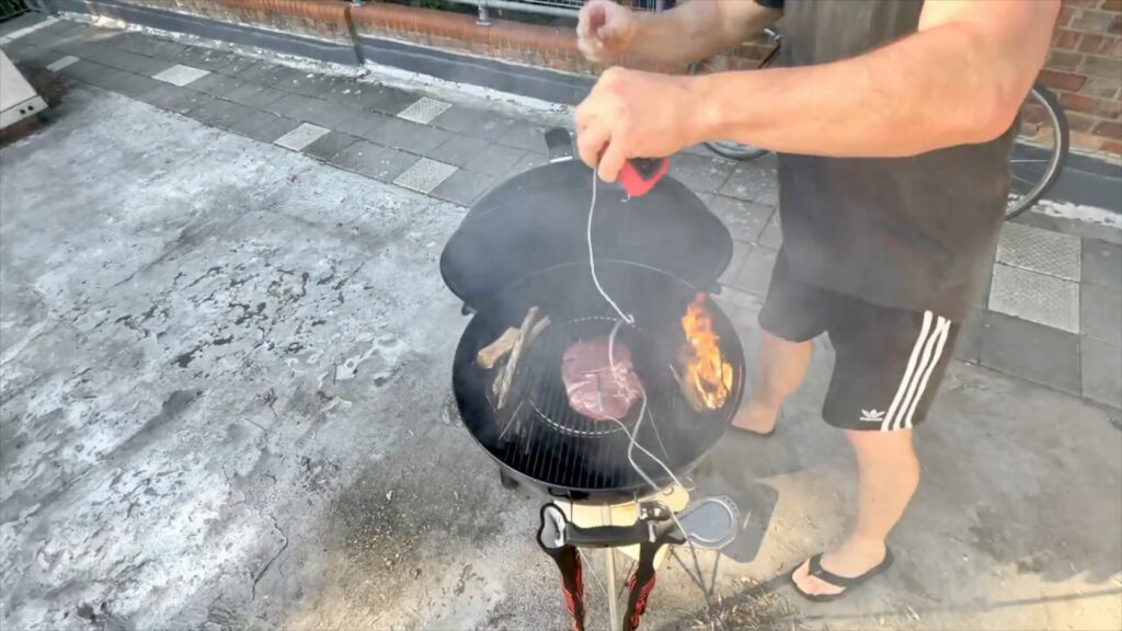 Smoke rising around lamb inside a Weber kettle barbecue on a London rooftop