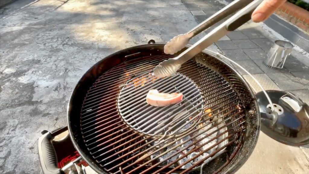 Pork belly cooking over charcoal with rosemary on a Weber kettle barbecue