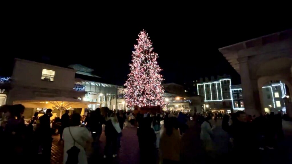 Illuminated Christmas tree in Covent Garden Piazza surrounded by the historic market buildings and evening visitors