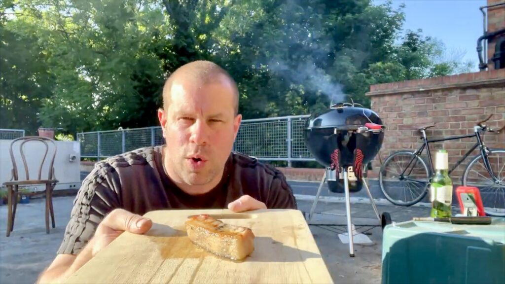 Barry Roberts tasting pork belly cooked with rosemary smoke on a rooftop barbecue