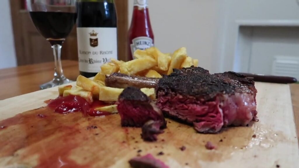 Sliced medium-rare bone-in rib steak served with chips after cooking at home