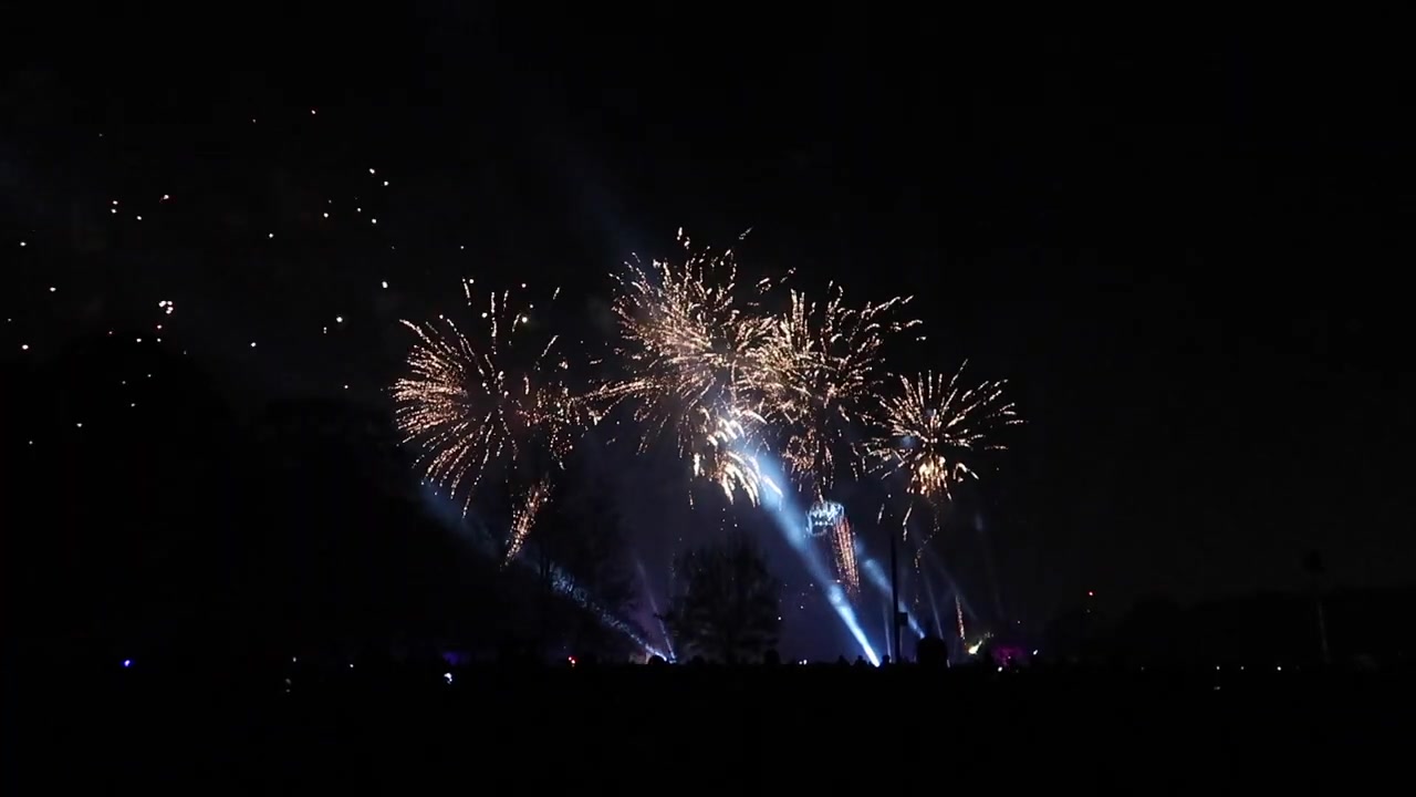 Blue searchlights and fireworks illuminating the sky above Victoria Park