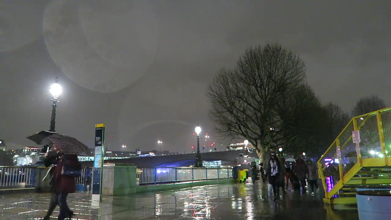 Pedestrians walking beside the Thames on a rainy South Bank evening