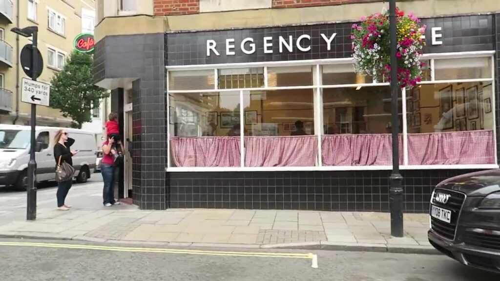 Black-tiled Regency Café exterior with white lettering and gingham curtains on Regency Street, Westminster.