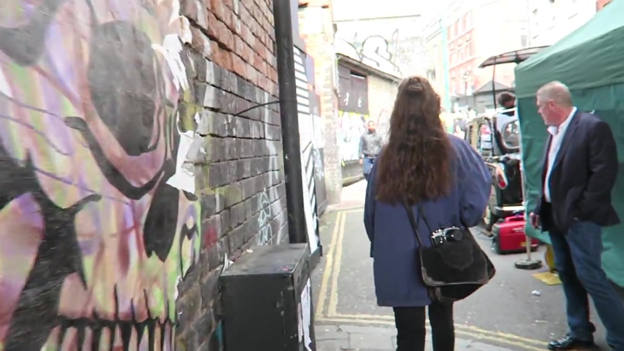 Large painted face on a brick wall beside a Brick Lane market passage