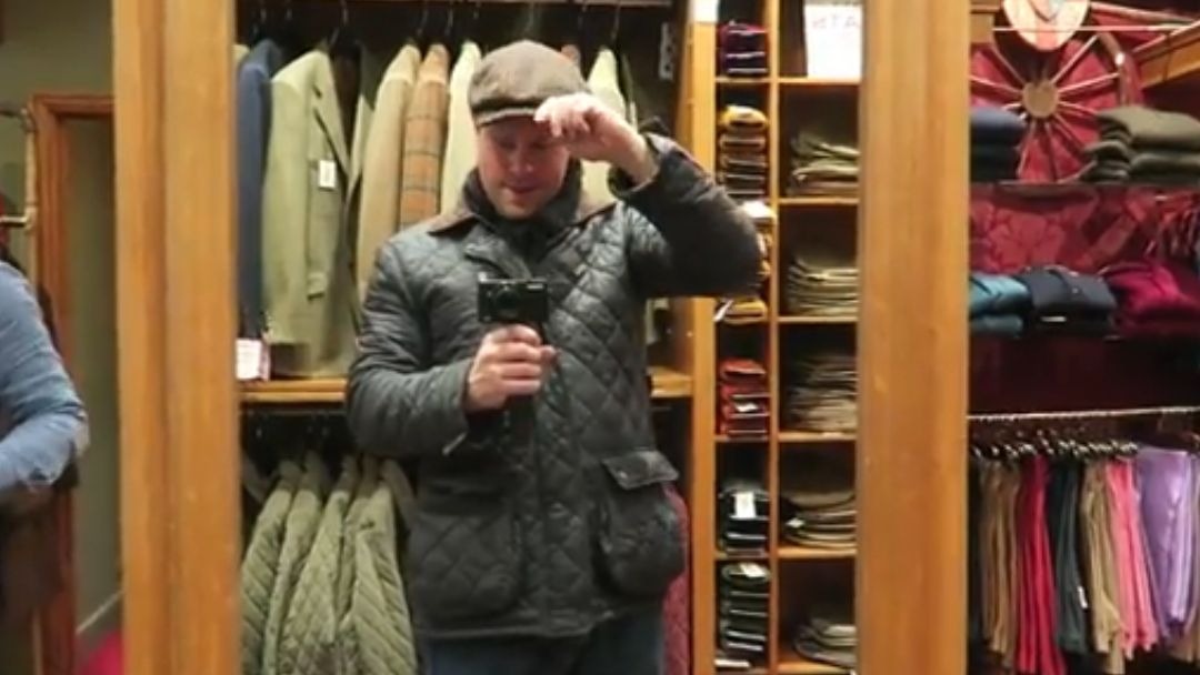 Barry Roberts trying on a grey flat cap inside Cordings of Piccadilly