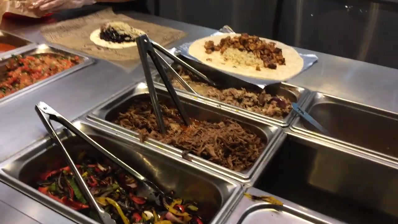 Grilled meat and vegetables being added to burritos at the counter