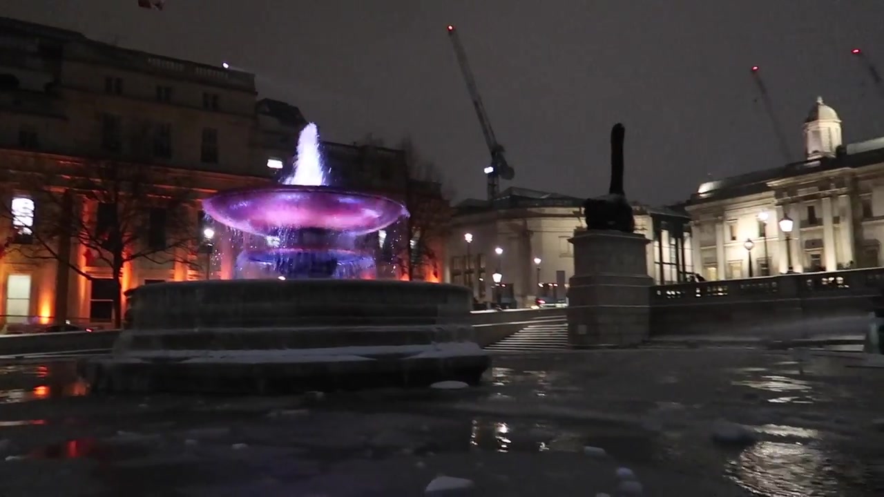 Illuminated fountain in Trafalgar Square on a snowy London night