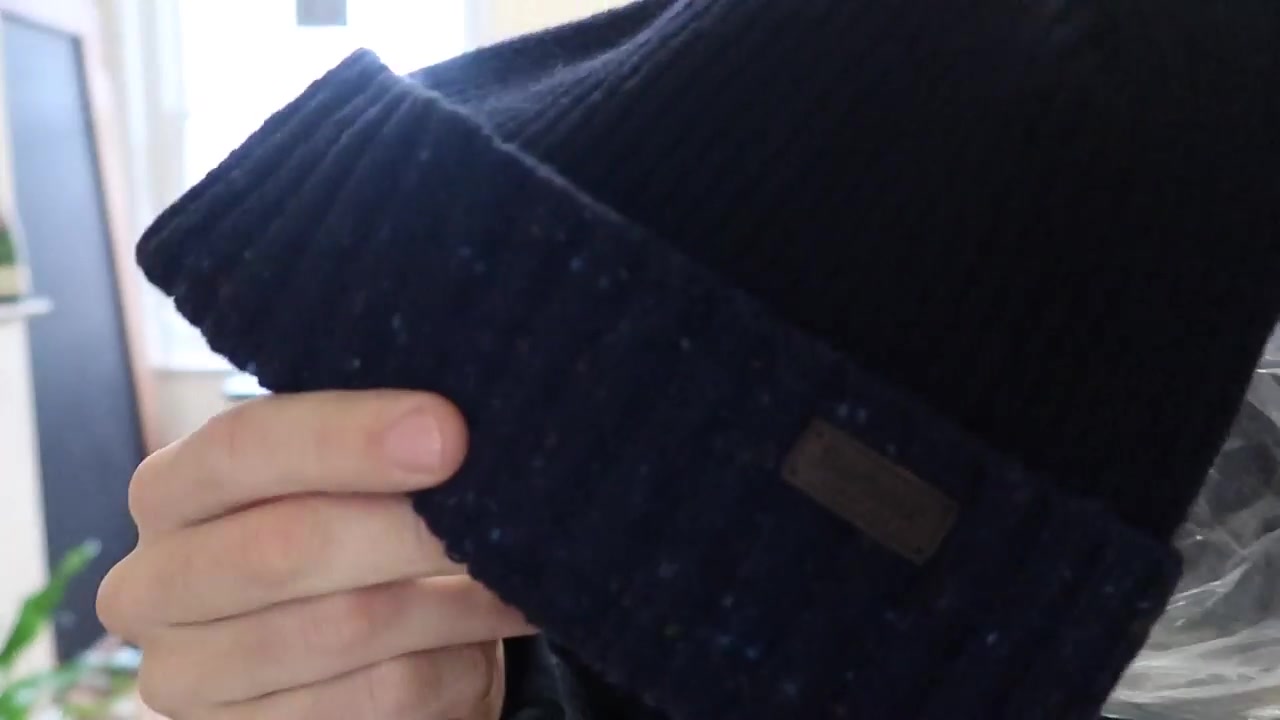 Navy Barbour flecked knitted pom hat held close to the camera during the Roberts London film.