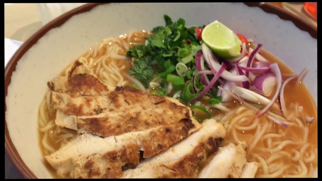 Bowl of ramen topped with grilled chicken, greens and red onion
