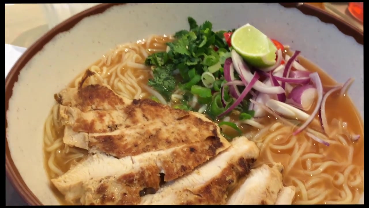 Bowl of ramen topped with grilled chicken, greens and red onion