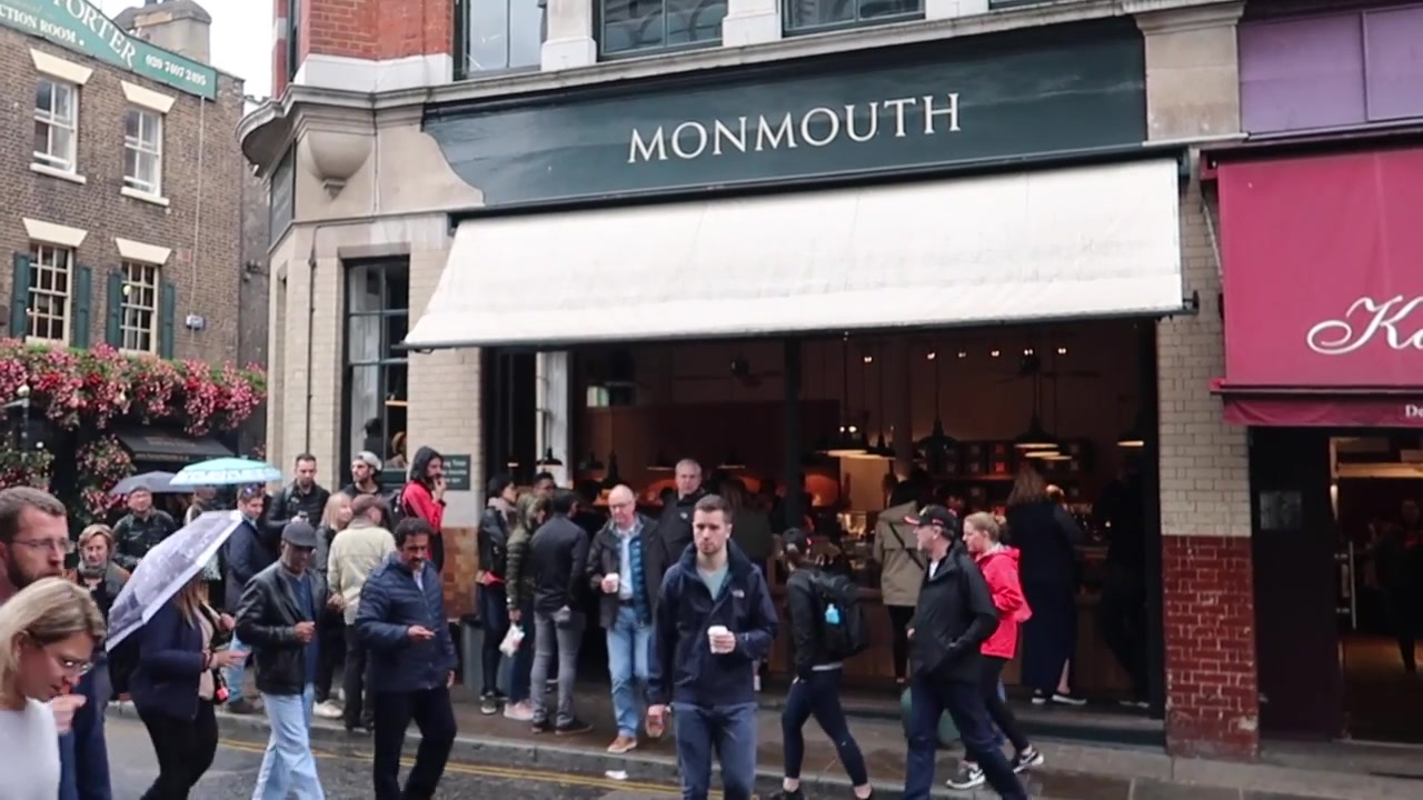 Front of Monmouth Coffee shop with customers queuing beneath umbrellas