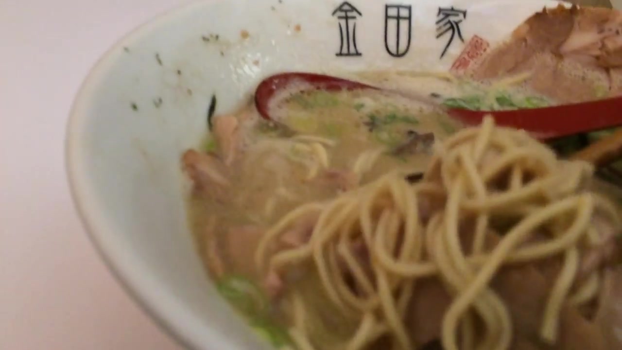 Thin ramen noodles being lifted from a bowl of cloudy tonkotsu broth at Kanada-Ya