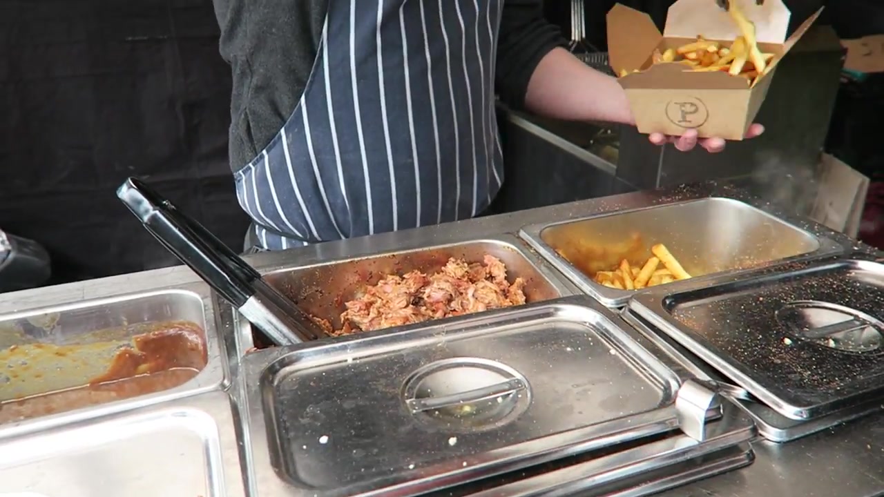 Trader preparing chips with cheese curds, gravy and rib meat at the Poutinerie