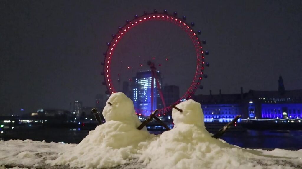 Two snow figures facing the illuminated London Eye across the Thames