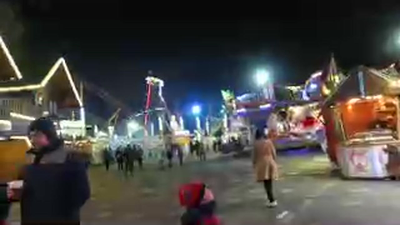 Visitors walking between illuminated fairground rides at Hyde Park Winter Wonderland 2015