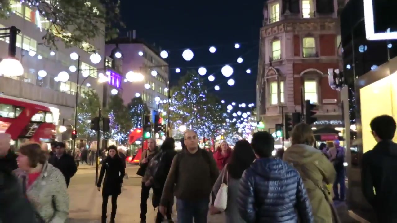 Christmas shoppers walking beneath white globe lights on Oxford Street in London.