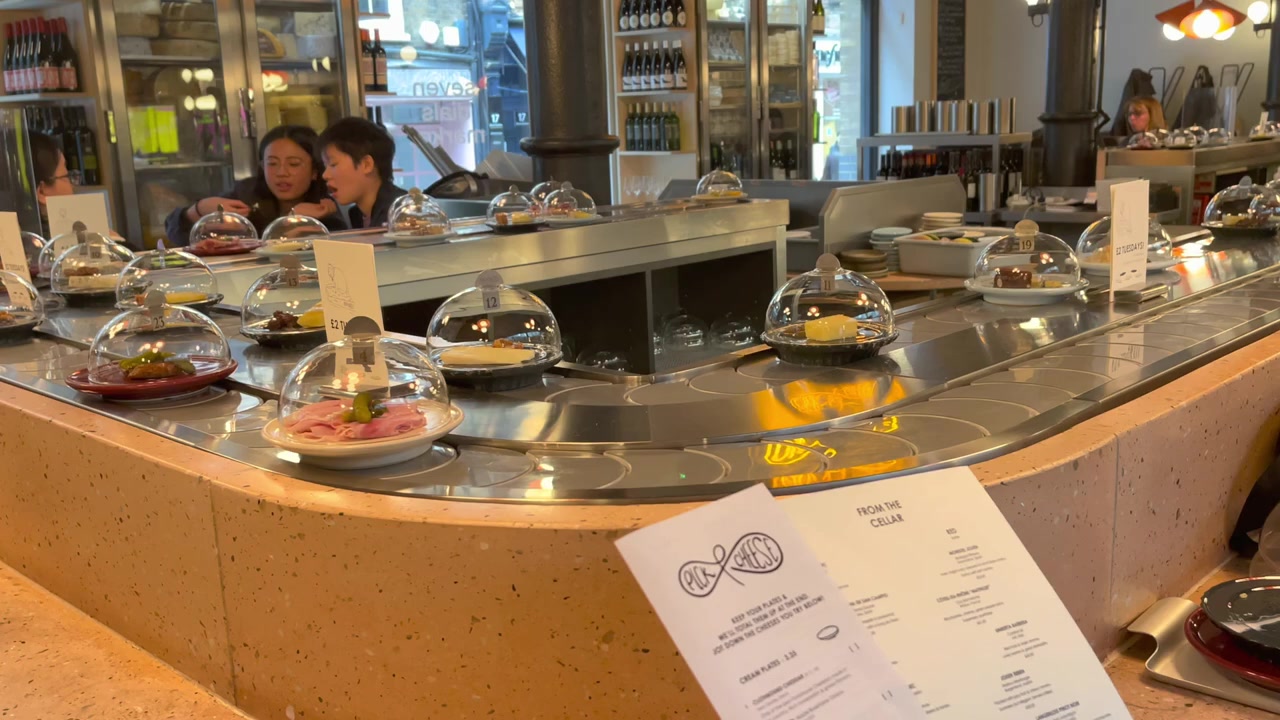Cheese plates under clear covers moving around the Pick & Cheese conveyor belt in Seven Dials Market.