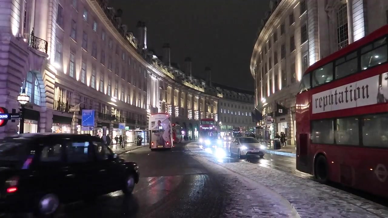Red London buses travelling along wet Regent Street after snowfall