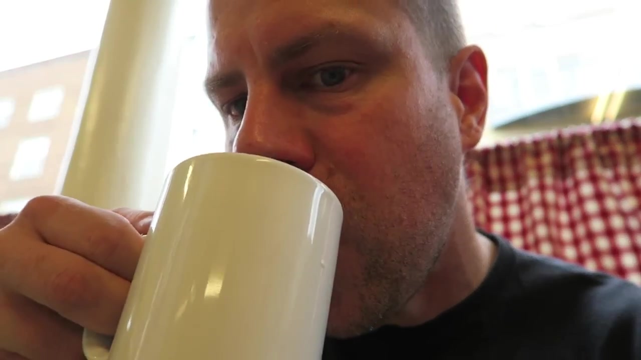 Barry Roberts drinking tea inside the Regency Café beside red gingham curtains.