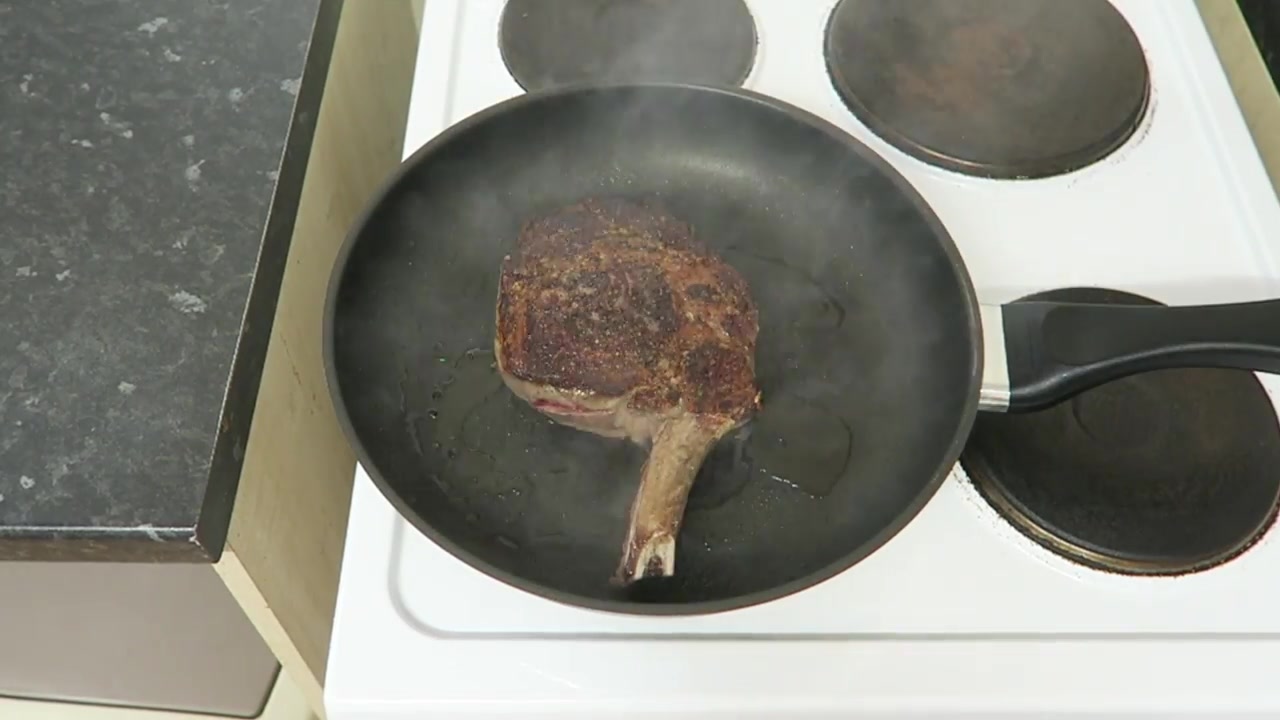 Browned bone-in rib steak being turned in a hot frying pan