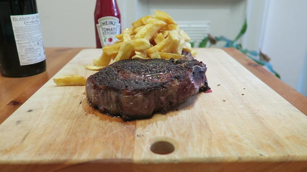 Cooked bone-in rib steak resting beside a serving of chips