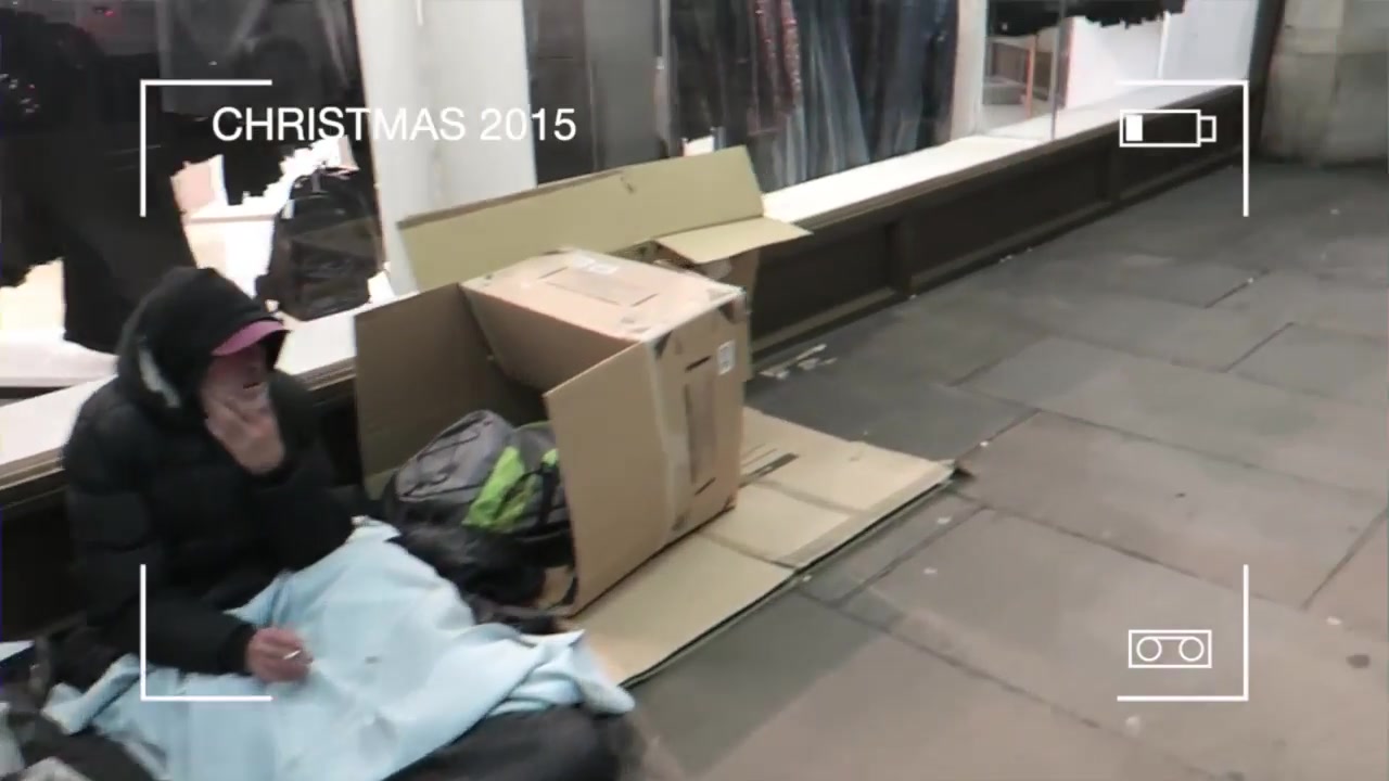 A person sleeping rough beneath blankets on a London street at Christmas