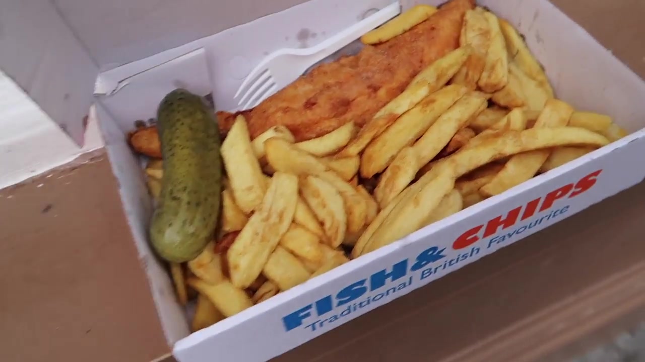 Box of British fish and chips with a pickled gherkin from Leather Lane