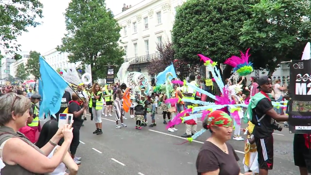 Feathered masquerade performers crossing the Notting Hill Carnival route