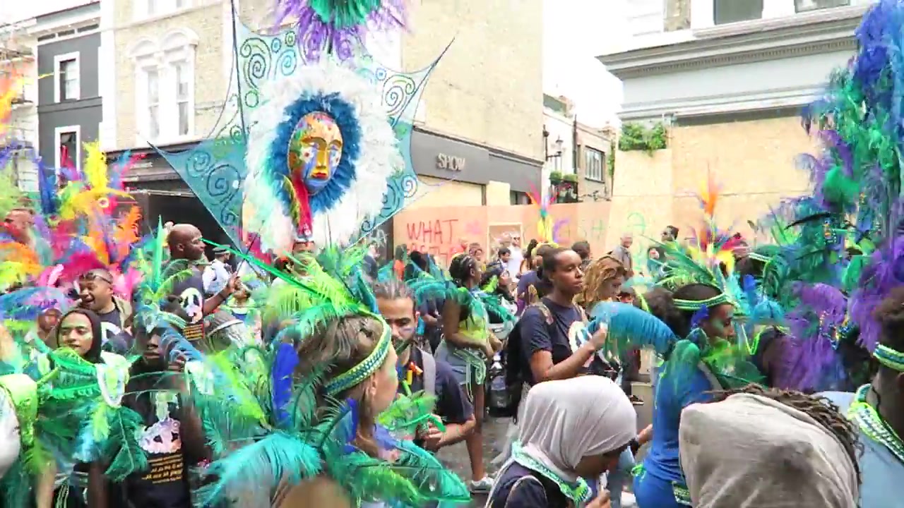 Masquerade performer in a vivid green and blue feathered costume at Notting Hill Carnival