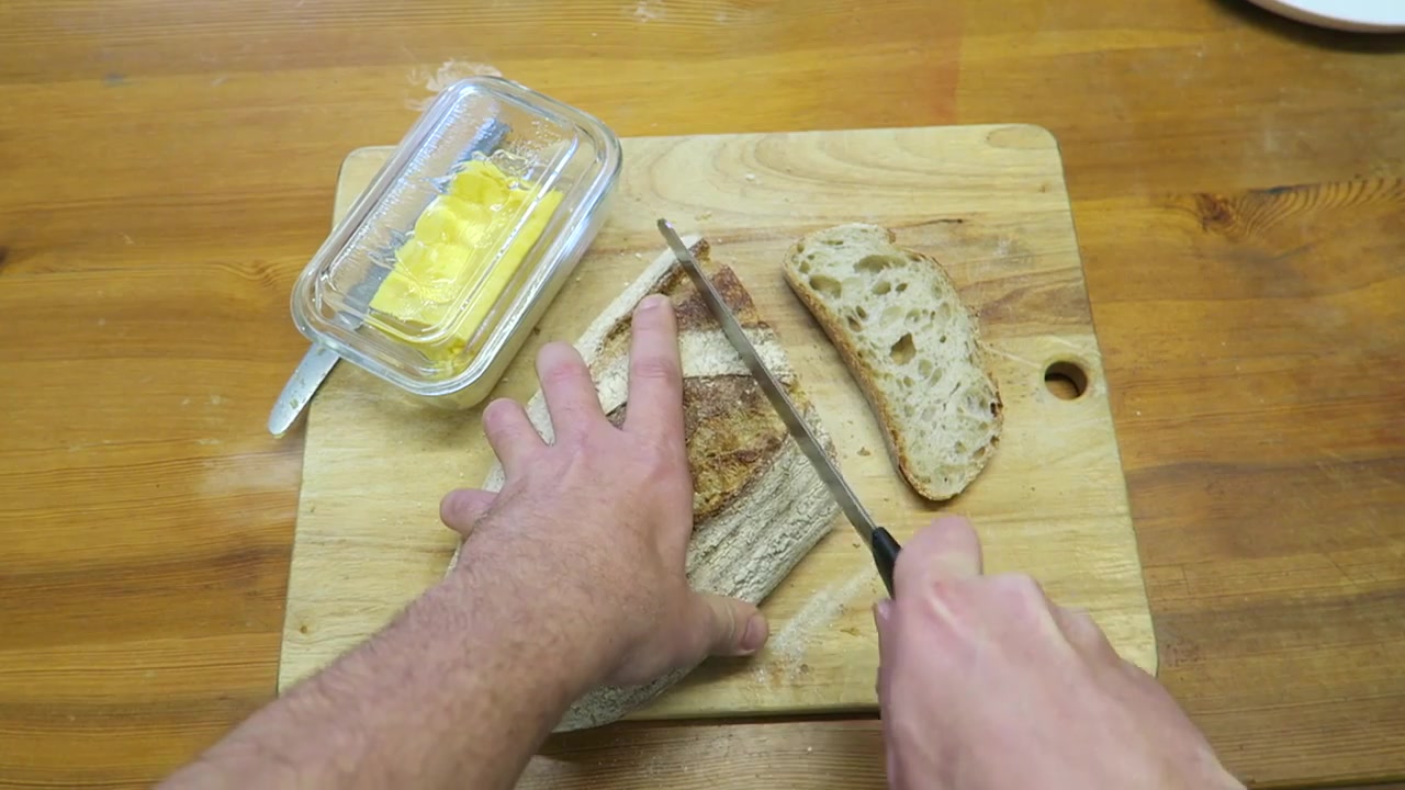 Thick slices of rustic bread being cut for a bacon sandwich