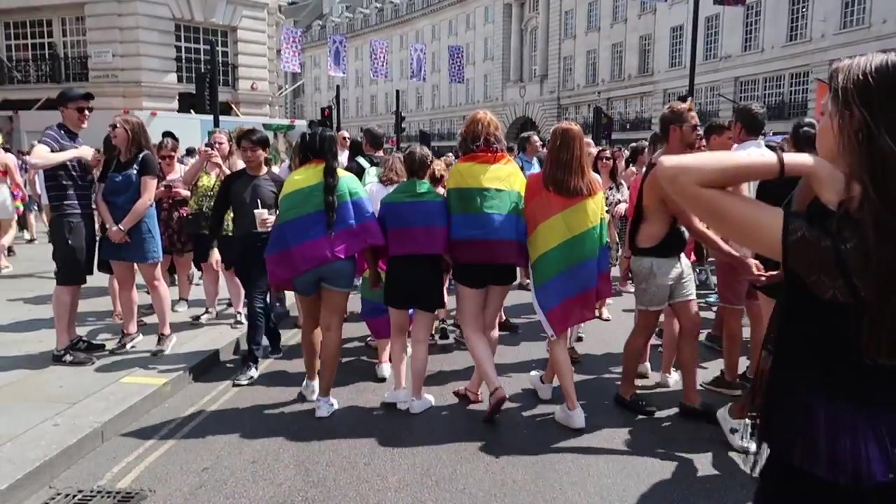 Four Pride in London attendees wearing rainbow flags beside the parade route