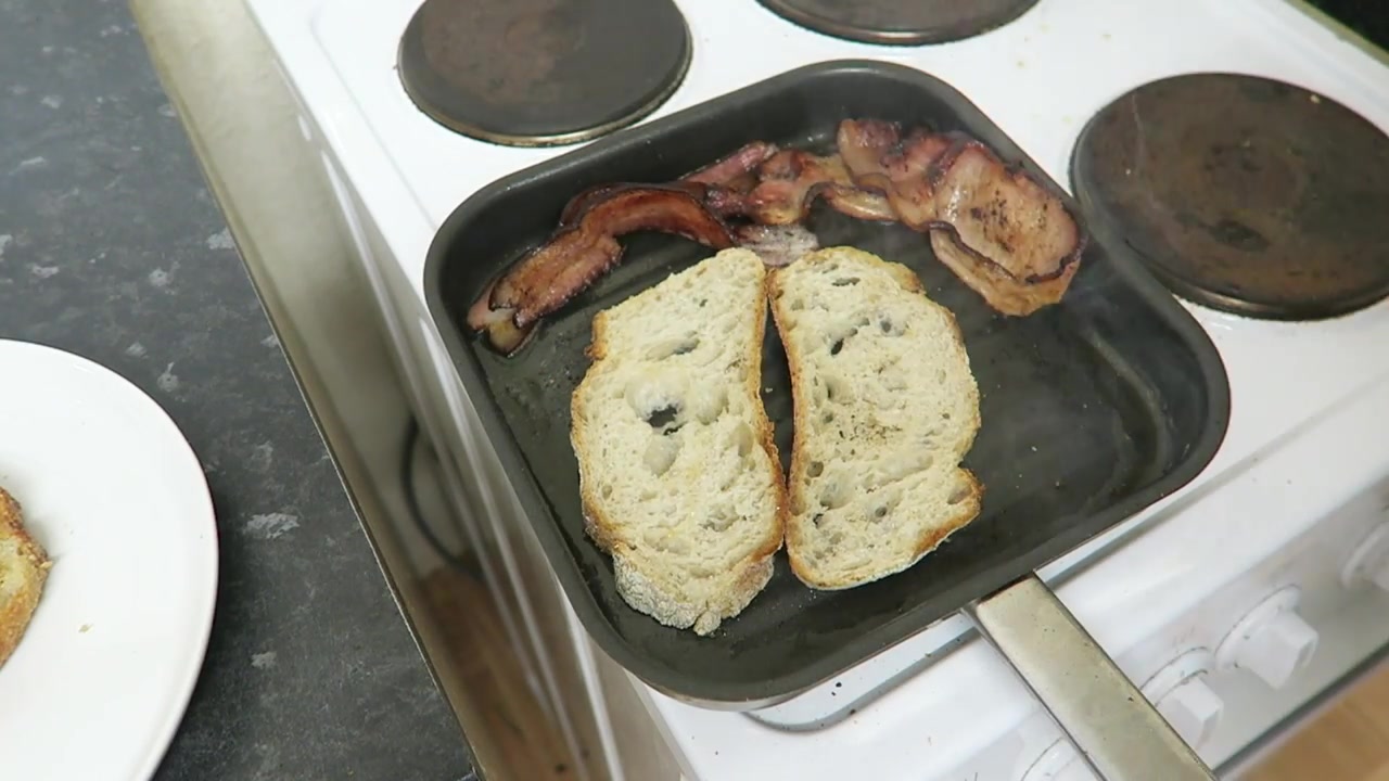 Rustic bread toasting beside cooked bacon in a griddle pan