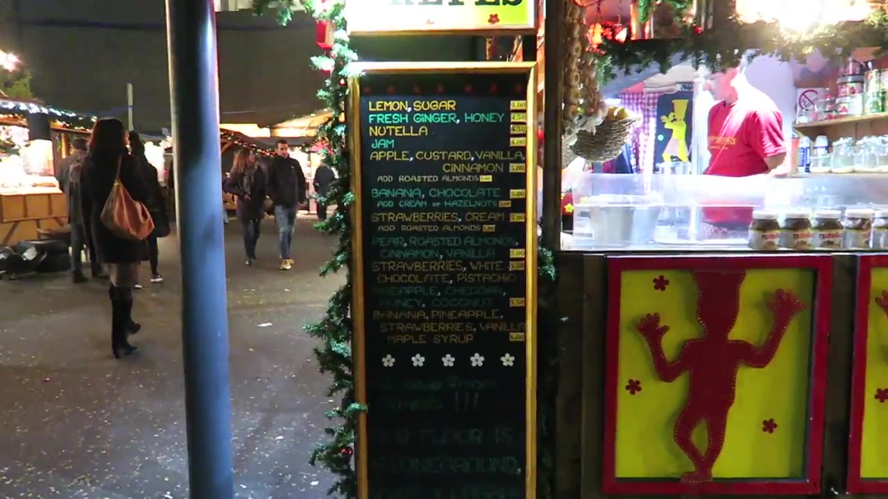 Food menu beside illuminated wooden chalets at London’s Southbank Christmas market