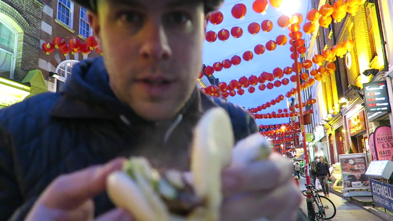 Barry holding a smaller Baozi Inn pork bun with greens beneath Chinatown lanterns