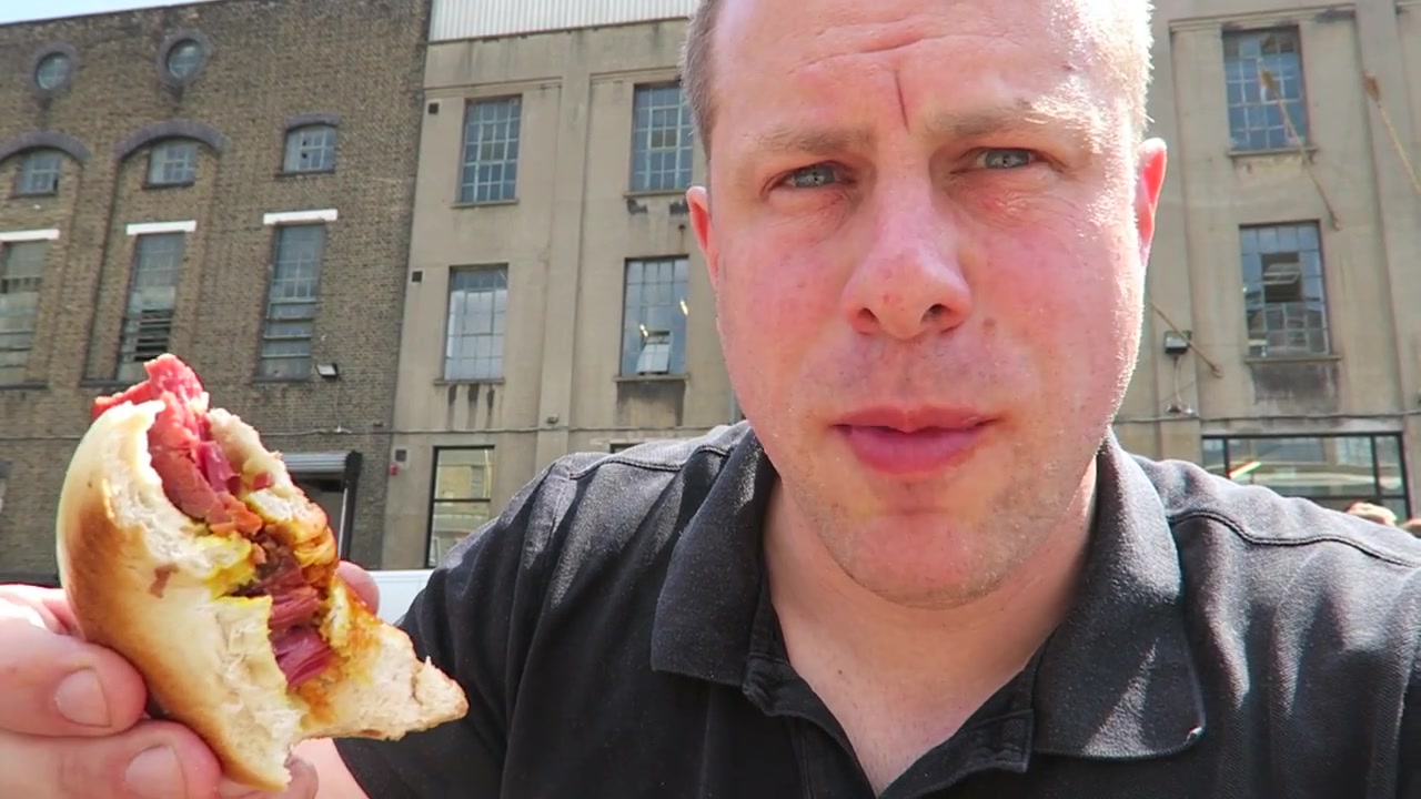 Barry holding a salt beef bagel while seated in the Truman Brewery yard