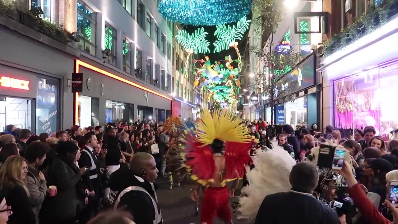 A crowd gathers around a dancer in a red and yellow feathered headdress.